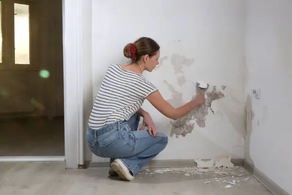 Personne grattant l'enduit décollé d'un mur humide au couteau à enduire